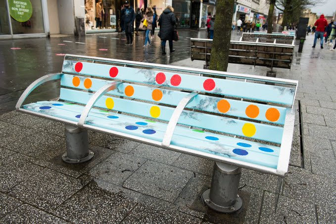 A white bench with multicoloured large dots on it that corresponds to a message in braille